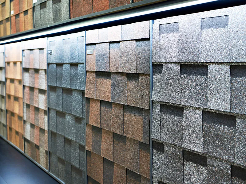 Display of architectural asphalt roofing shingle samples in brown and gray tones, textured overlapping squares