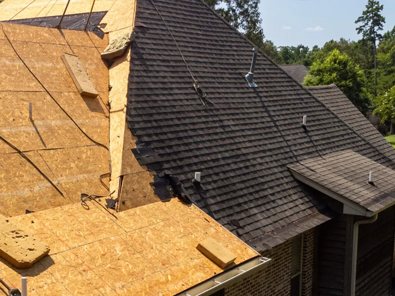 Residential roof under repair: exposed plywood decking, new asphalt shingles, flashing and vents.